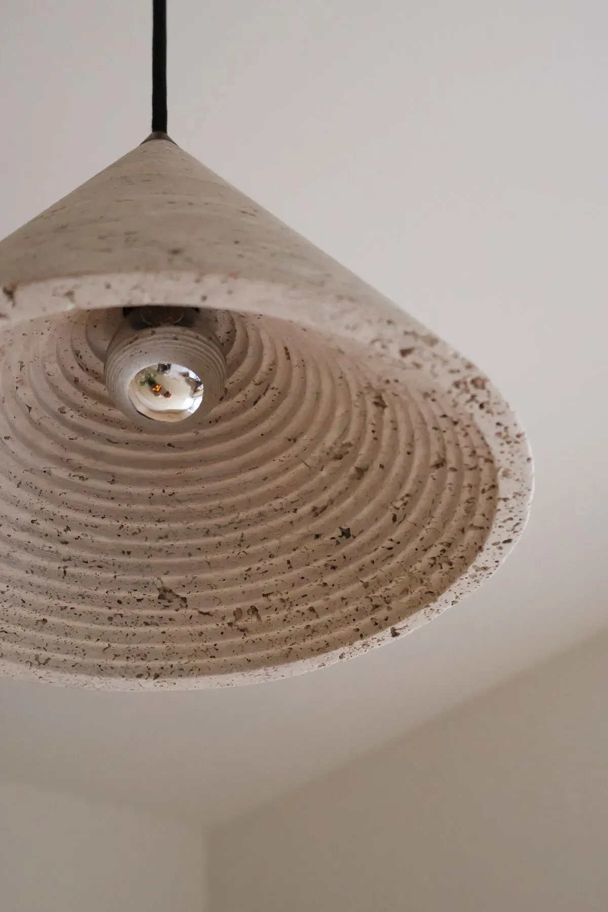 Modern concrete pendant light fixture with circular concentric design and black cord against white ceiling