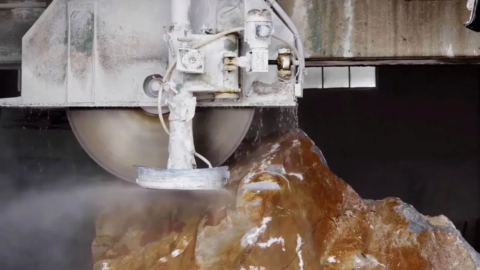 Water jet cutting equipment slicing through brown stone material with spray mist