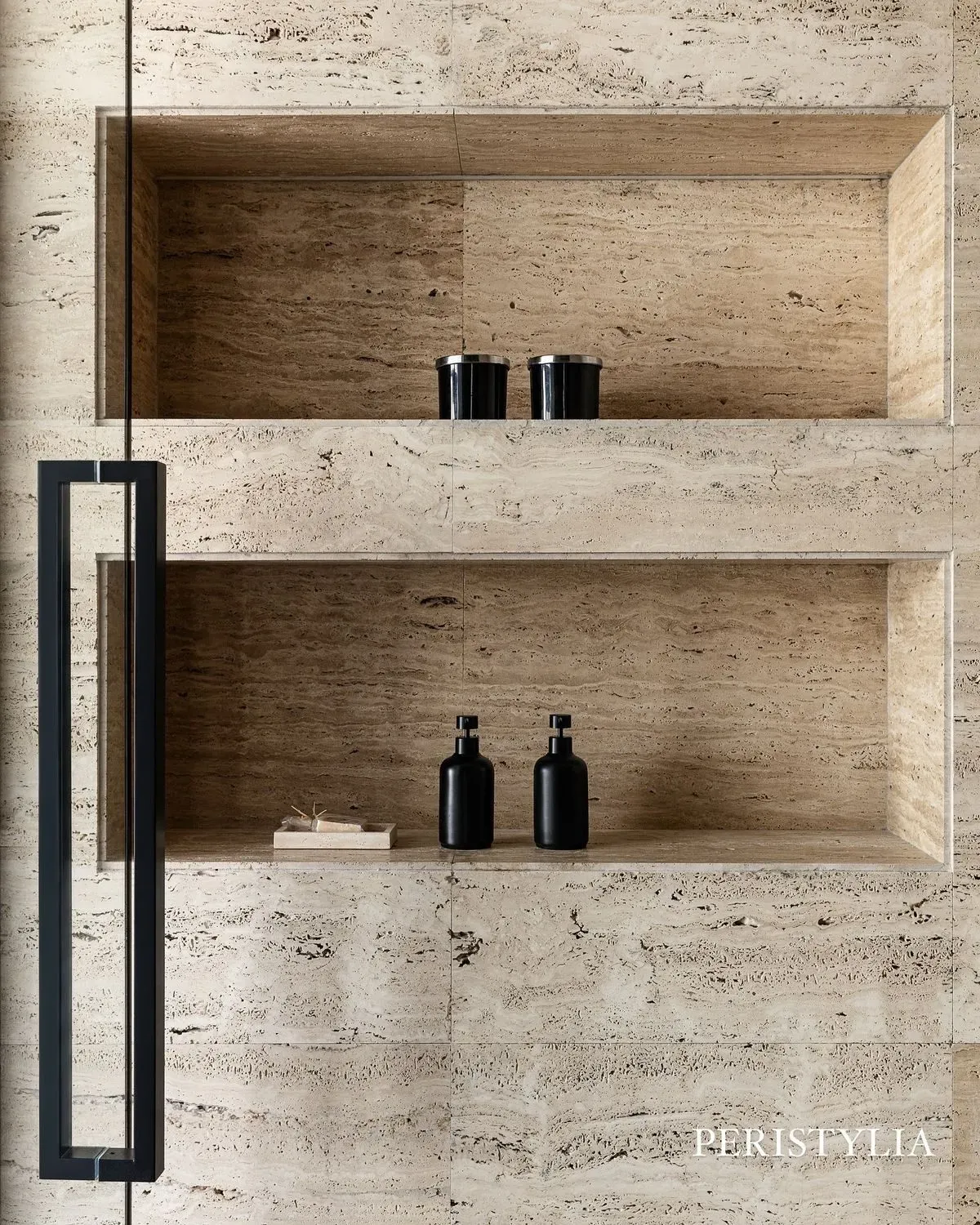 Recessed shelving in travertine stone wall with black metal frame and decorative bottles